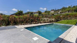 Una piscina rectangular con superficie de agua azul cristalina, rodeada por un solárium de piedra y una zona ajardinada.