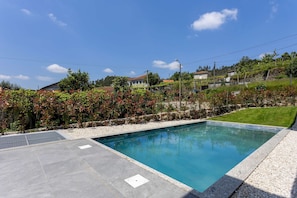 A rectangular swimming pool with a clear blue water surface, surrounded by a stone deck and a grassy area. - Casa do Bacelar by Liiiving (Fafe)