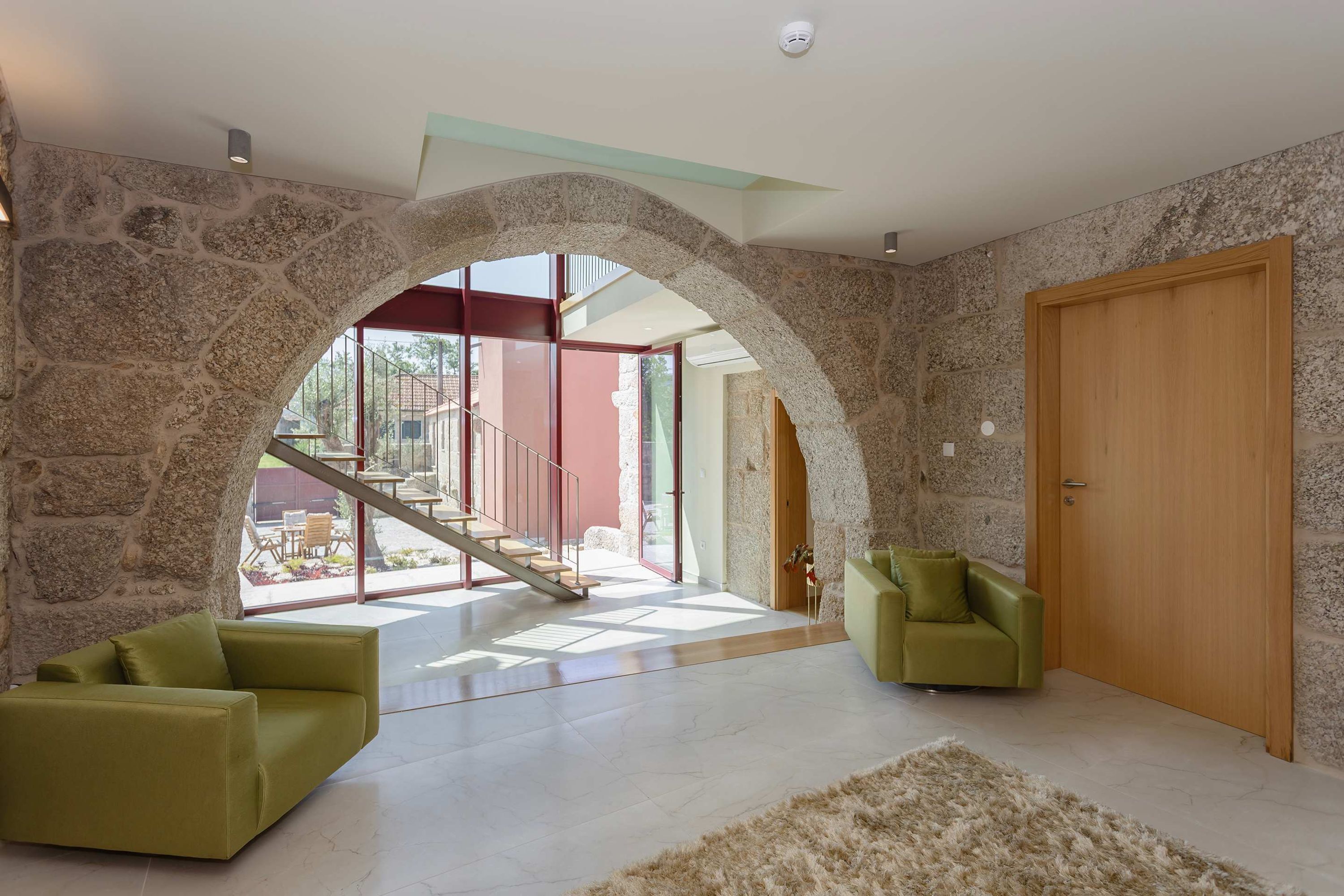 Amplia sala de estar con un arco de piedra que da a un balcón, una puerta de madera y una escalera.