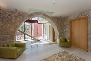 A spacious living area with a stone archway leading to a balcony, a wooden door, and a staircase. - Casa do Bacelar by Liiiving (Fafe)