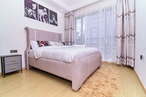 A bedroom with a bed, a nightstand, a fluffy rug, and a window with curtains. - Leshwa House 1 is situated in the high end of Nairobi with tranquil and Ambience (Nairobi)