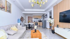 Uma sala de estar moderna com sofá, mesa de centro, lustre, espaço para refeições, cozinha e TV.