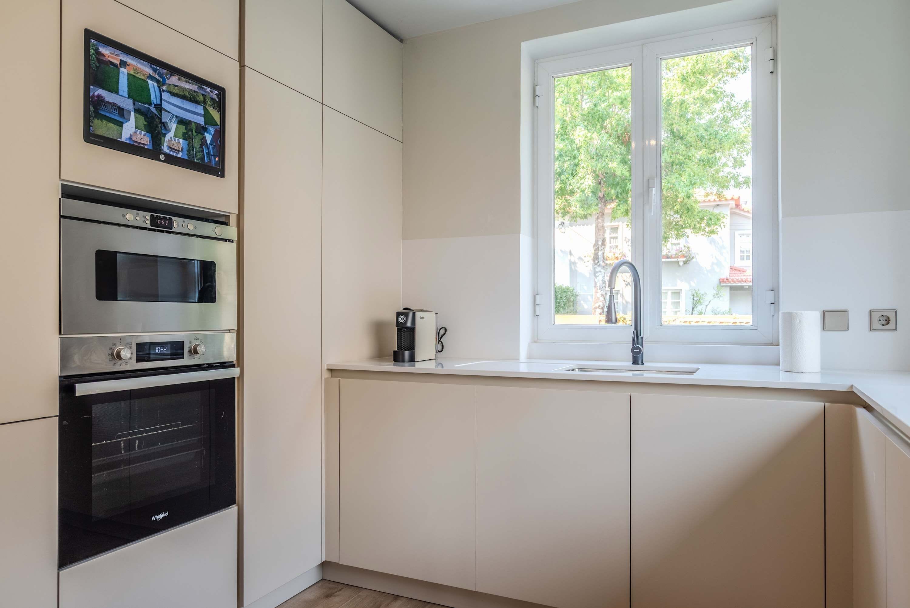 A kitchen with a built-in oven, a coffee maker, and a window with a view of the outside.