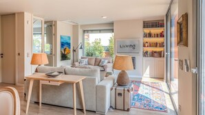 Ein modernes Wohnzimmer mit einer Sofagarnitur, einem Tisch mit einer Schale, Lampen, einem Teppich und einem Bücherregal.