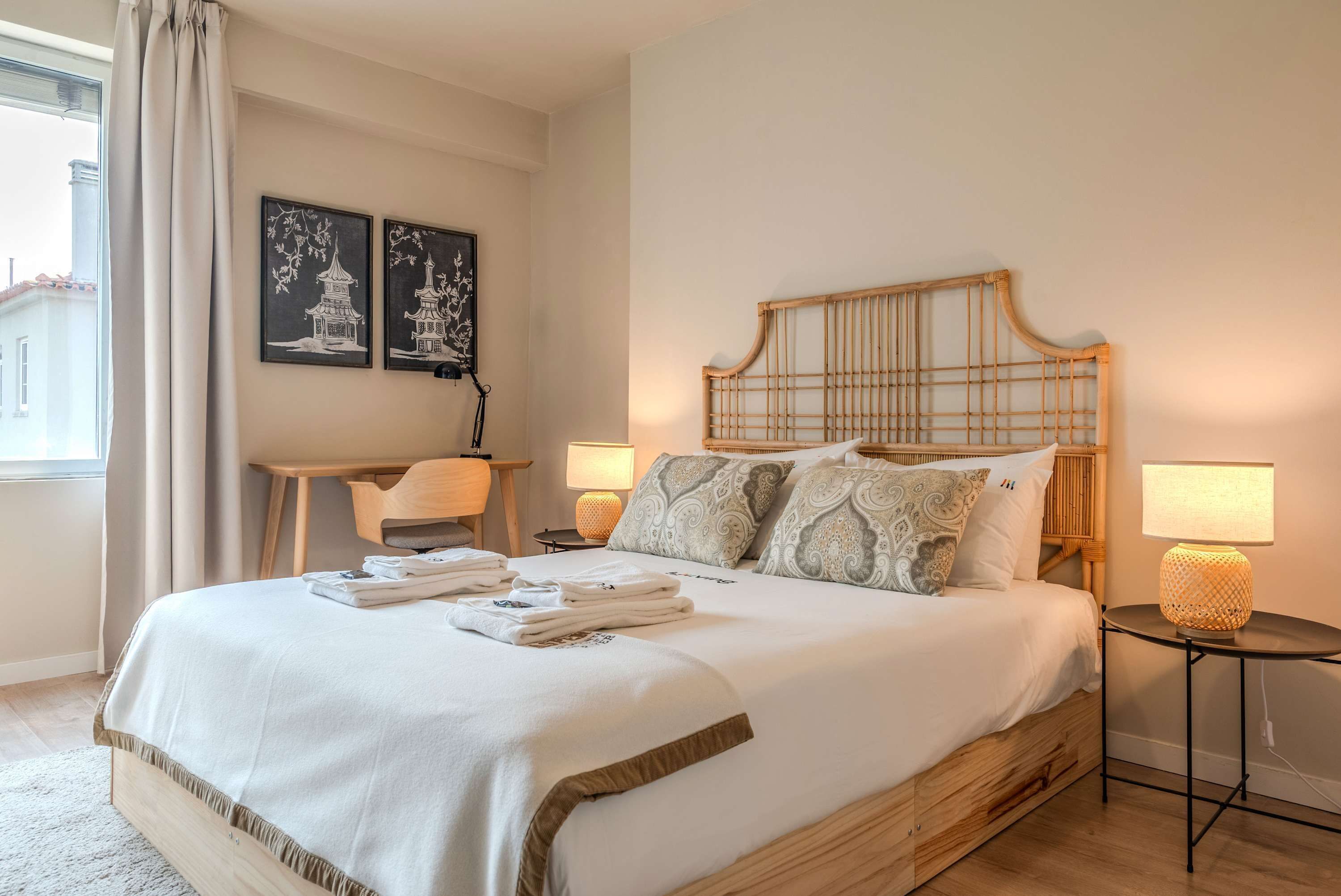 A neatly made bed with a headboard, two bedside lamps, a chair, and artwork on the wall.