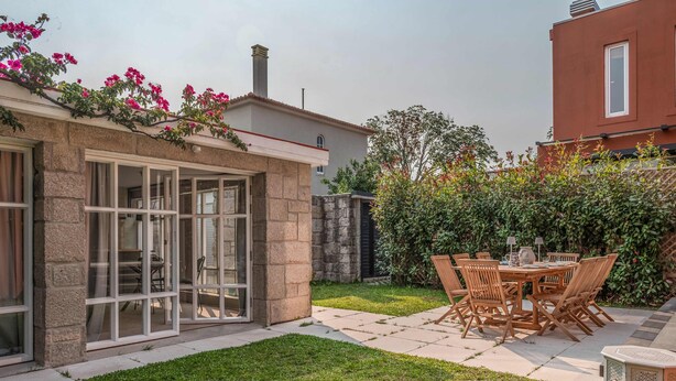 Eine Terrasse mit Tisch und Stühlen, eine Rasenfläche und ein Gebäude mit einer Steinaußenwand.