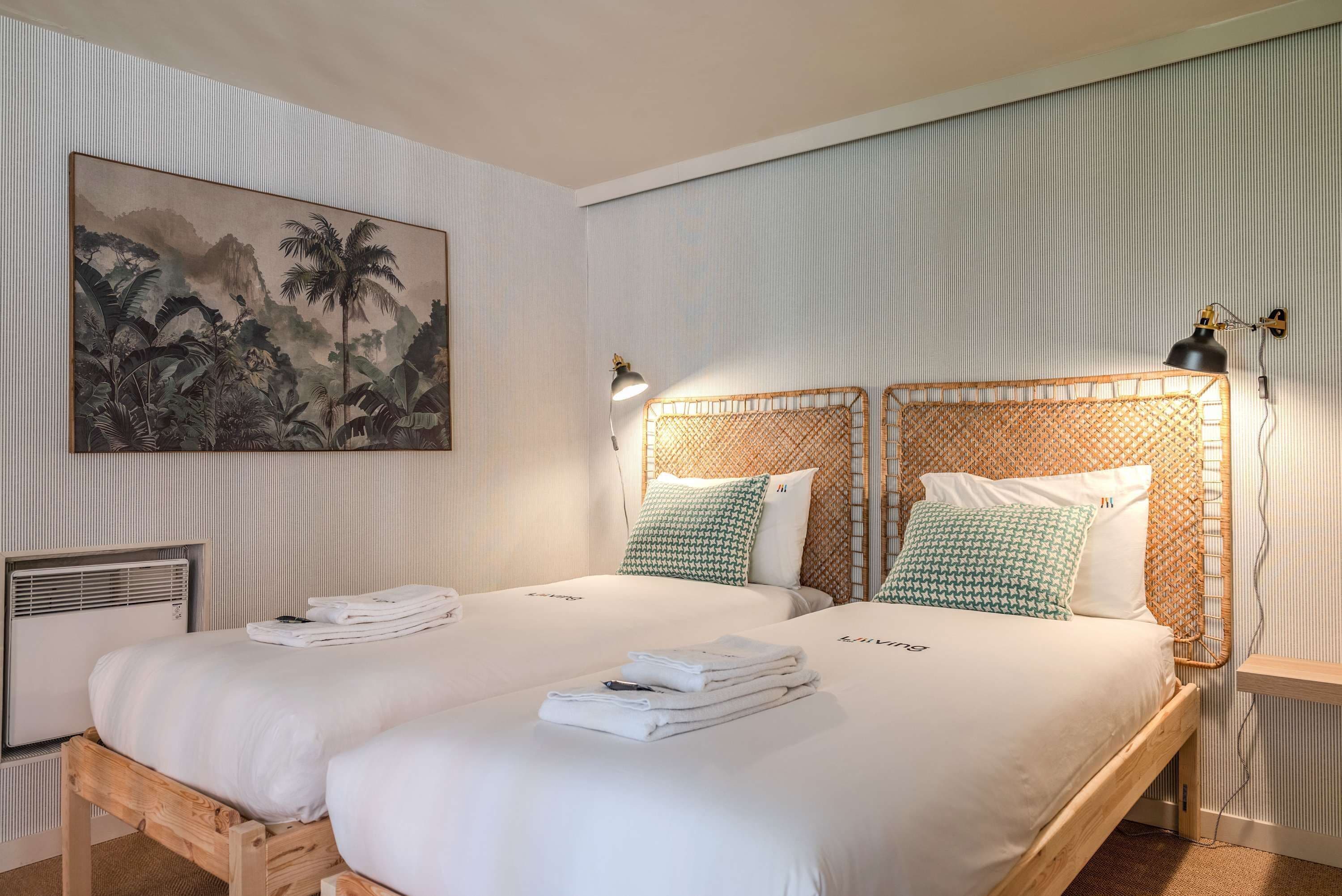 A hotel room with two beds, a large painting on the wall, and a small table with a lamp.