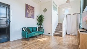 A room with a teal sofa, a plant, a staircase, and a TV on a wooden stand. - Twin Bed Studio Apartment | Coventry CV2| Parking (Coventry)
