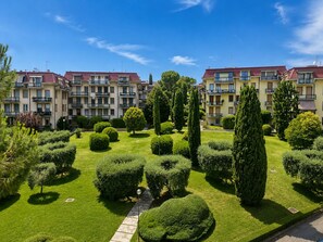 A residential building with multiple balconies, a well-maintained garden with various shrubs and trees, and a clear blue sky. - Casa delle anatre By Case al Lago (Desenzano del Garda)