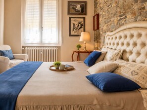 A bedroom with a large bed, a radiator, a window with blinds, a lamp, and a stone wall. - Casa delle anatre By Case al Lago (Desenzano del Garda)