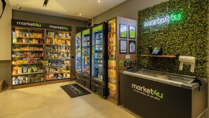 A grocery store interior with refrigerated sections, shelves stocked with products, and a neon sign. - StayHome Moema NexOne Pool & Gym (São Paulo)