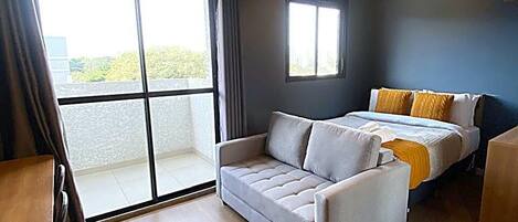 Un dormitorio con cama, sofá, ventana y ventilador de techo.