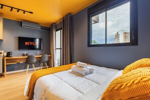 A modern hotel room with a bed, a desk with chairs, a TV, and a large window. - StayHome Moema NexOne Pool & Gym (São Paulo)