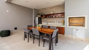 A modern kitchen with a wooden dining table, grey chairs, a built-in oven, and a stone backsplash. - StayHome Moema NexOne Pool & Gym (São Paulo)