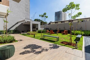 A courtyard with a wooden deck, outdoor seating, and young trees. - StayHome Moema NexOne Pool & Gym (São Paulo)
