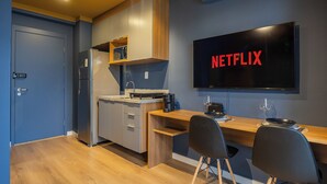 A modern kitchen with a built-in refrigerator, microwave, and wooden cabinets. A flat-screen TV mounted on the wall displays 'NETFLIX'. - StayHome Moema NexOne Pool & Gym (São Paulo)