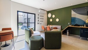 A modern office space with a glass door leading outside, a reception desk, and a seating area with a green wall and circular light fixtures. - StayHome Moema NexOne Pool & Gym (São Paulo)