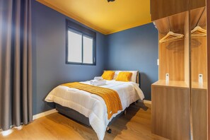Een slaapkamer met een bed, raam, kledingkast en nachtkastje.