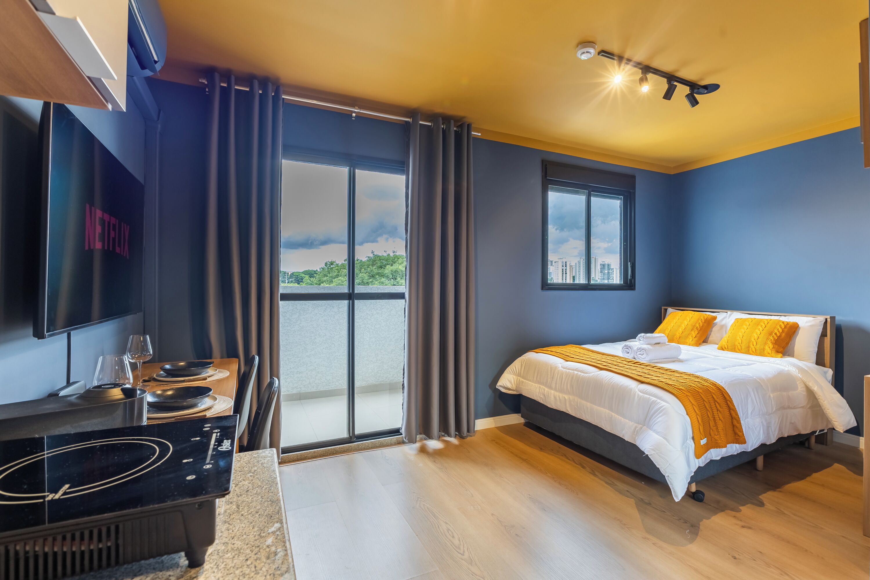 Una habitación de hotel moderna con cama, televisor y balcón con vista a la ciudad.