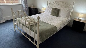 Una cama individual con estructura metálica, una mesita de noche, una lámpara y una ventana con cortinas.