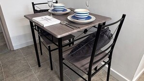 Una mesa de comedor dispuesta con platos, tazones y cubiertos, junto a una silla y un cojín en el suelo.