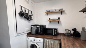 Cocina compacta con lavadora, microondas, hervidor y utensilios de cocina colgando.