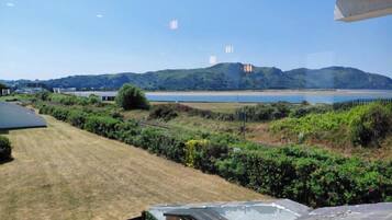 A view from a covered outdoor area with a lawn, a fence, and a body of water in the background.
