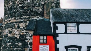 Ein historischer Steinturm neben einem traditionellen Gebäude in Schwarz und Weiß mit einer roten Tür, beschriftet mit 'The Smallest House in Great Britain'.