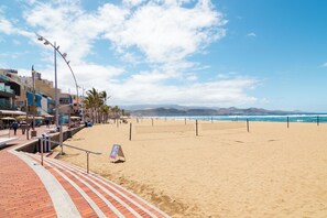 A beach with a paved walkway, a signboard, and buildings in the background. - Solajero Apartment in Las Canteras (Las Palmas de Gran Canaria)