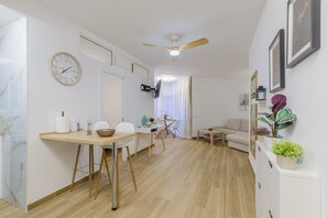 A modern living room with a dining area, a ceiling fan, a clock, and a sofa. - Solajero Apartment in Las Canteras (Las Palmas de Gran Canaria)