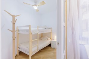 A bunk bed room with a ceiling fan, a bedside table with a lamp, and a door with a curtain. - Solajero Apartment in Las Canteras (Las Palmas de Gran Canaria)