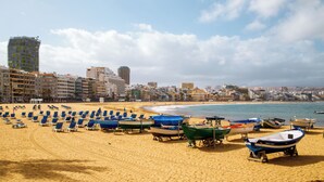 Una spiaggia con file di lettini e diverse barche.