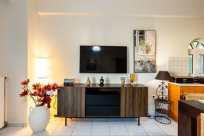 Ein modernes Wohnzimmer mit Flachbildfernseher, einer Holzkommode, einer weißen Vase mit Blumen und einem kleinen Tisch mit Lampe.