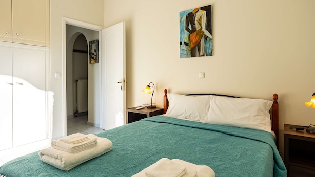 A bedroom with a bed, a nightstand, a lamp, a painting, and a wardrobe. - Kyparissia Modern Home Serene Views Calm Vibes (Trifylia)