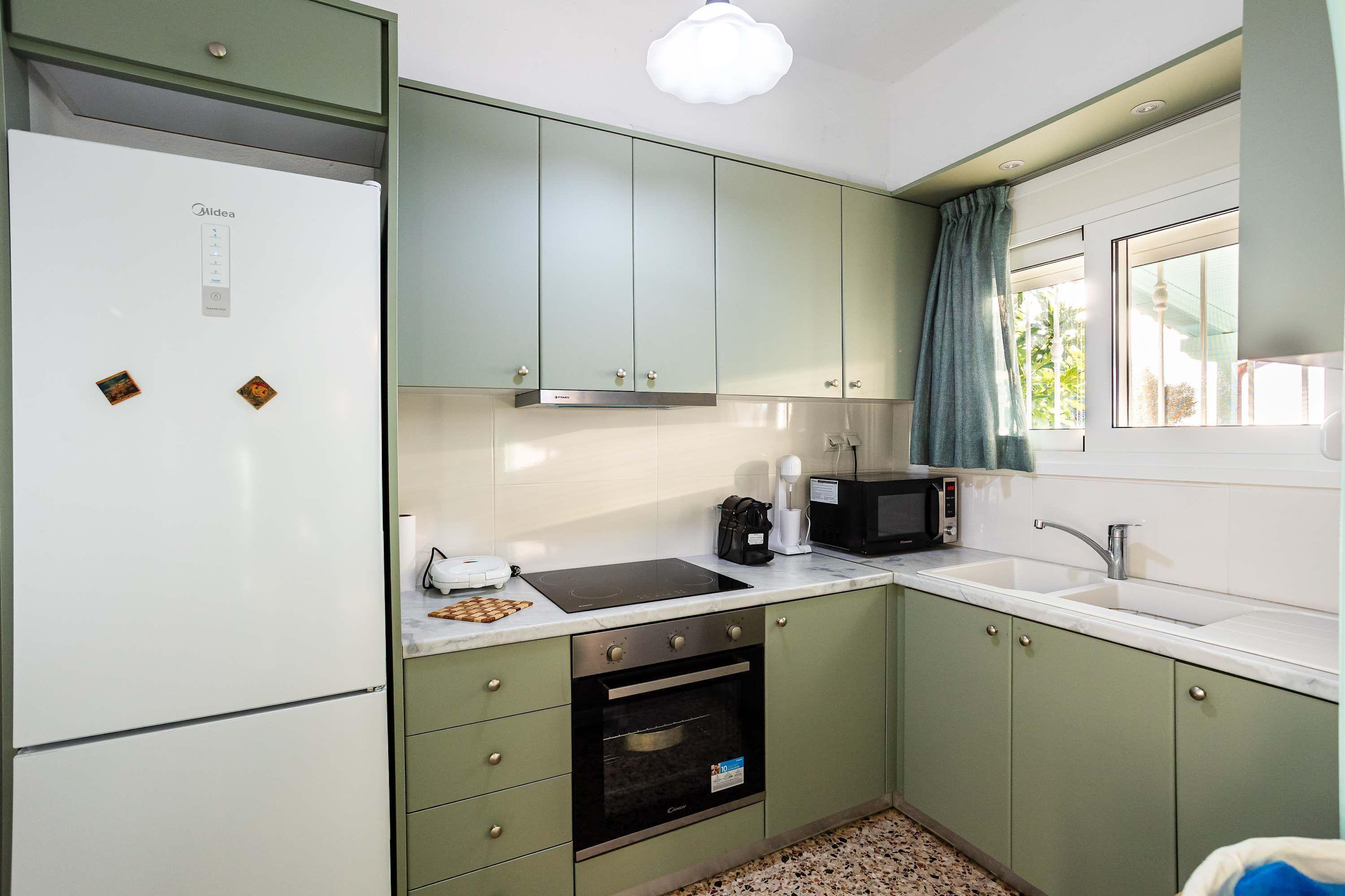 Une cuisine compacte équipée d’un réfrigérateur, d’une cuisinière, d’un four, d’un four à micro-ondes et d’une fenêtre avec des rideaux.