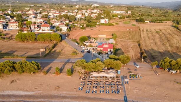Vista aerea di una zona costiera con una spiaggia, una fila di case e un edificio con tetto rosso.