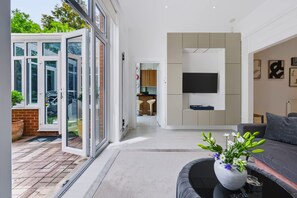 A modern living room with a sofa, a coffee table, and a TV mounted on the wall. - Garden Apartment Escape in Hampstead (London)