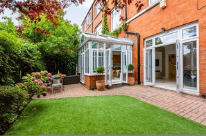 Ein Wohnhaus mit Wintergarten, einer Terrasse mit Tisch und Stühlen und einem gepflegten Rasen.