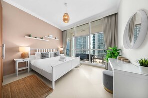 A modern bedroom with a bed, bedside tables, a dresser, a large window with curtains, and a view of high-rise buildings. - Free Housekeeping Visits During Your Stay - Stayshort - Elegant 4 Bedroom in Dubai Marina That Sleeps 10 (Dubai)