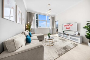 A modern living room with a sofa, a coffee table, a TV, and a bookshelf. - Free Housekeeping Visits During Your Stay - Stayshort - Elegant 4 Bedroom in Dubai Marina That Sleeps 10 (Dubai)