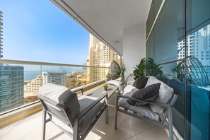 A balcony with a view of a cityscape, including high-rise buildings and a body of water. There are two chairs and a small table with a plant. - Free Housekeeping Visits During Your Stay - Stayshort - Elegant 4 Bedroom in Dubai Marina That Sleeps 10 (Dubai)