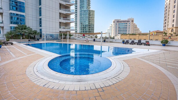 Una piscina con diseño circular, rodeada por un solárium con baldosas.