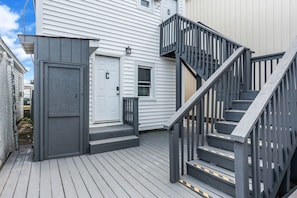 En uteplats vid ett bostadshus med en trätrappa och en dörr som är märkt med bokstaven ”C”.
