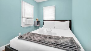 Ein Schlafzimmer mit einem Bett, zwei Wand-Klimaanlagen, einem Nachttisch mit Lampe und einer grauen Decke.