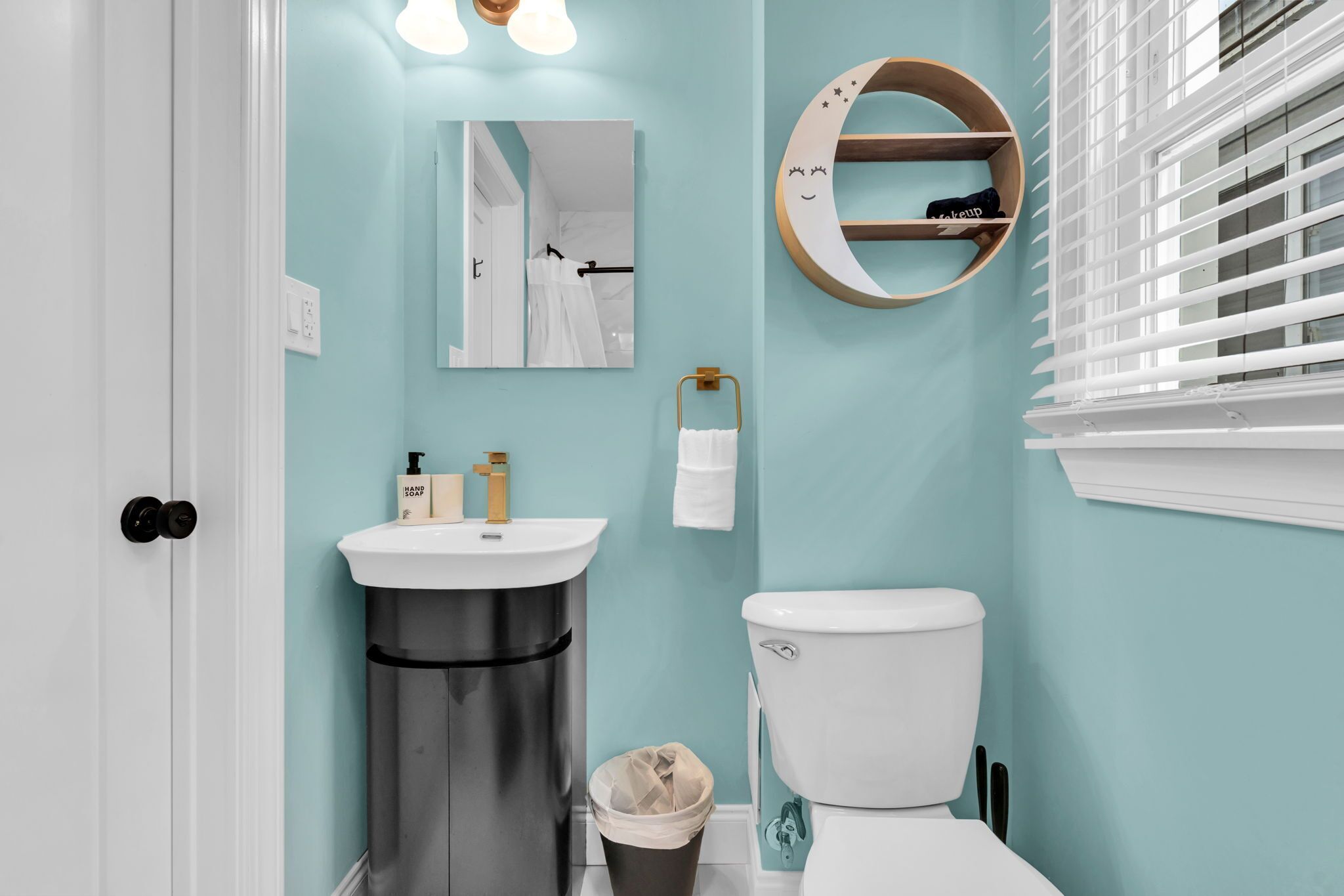 A bathroom with a sink, toilet, mirror, and a moon-shaped shelf.
