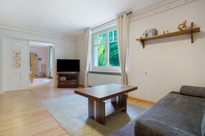 A living room with a wooden table, a grey sofa, a television, and a bookshelf. - Apartment 'Idylle Ostsee' – Buddenhagen, Gateway to Usedom Island (Wolgast)