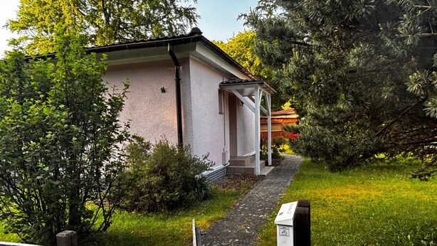 A building with a paved pathway leading to a wooden door, surrounded by greenery and trees. - Apartment 'Idylle Ostsee' – Buddenhagen, Gateway to Usedom Island (Wolgast)