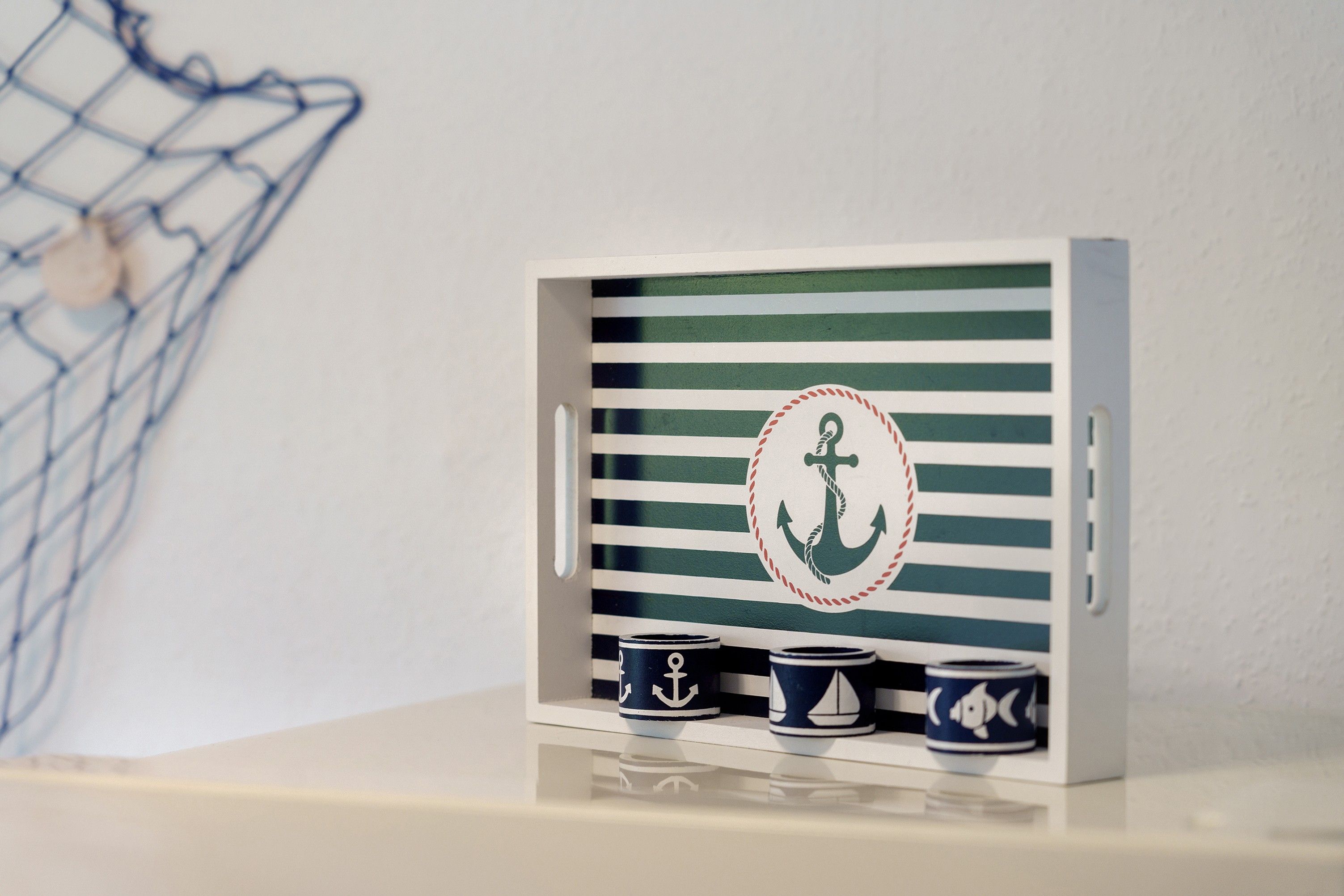 Een zeetje-decoratie met een gestreepte achtergrond, een anker en drie mokken.