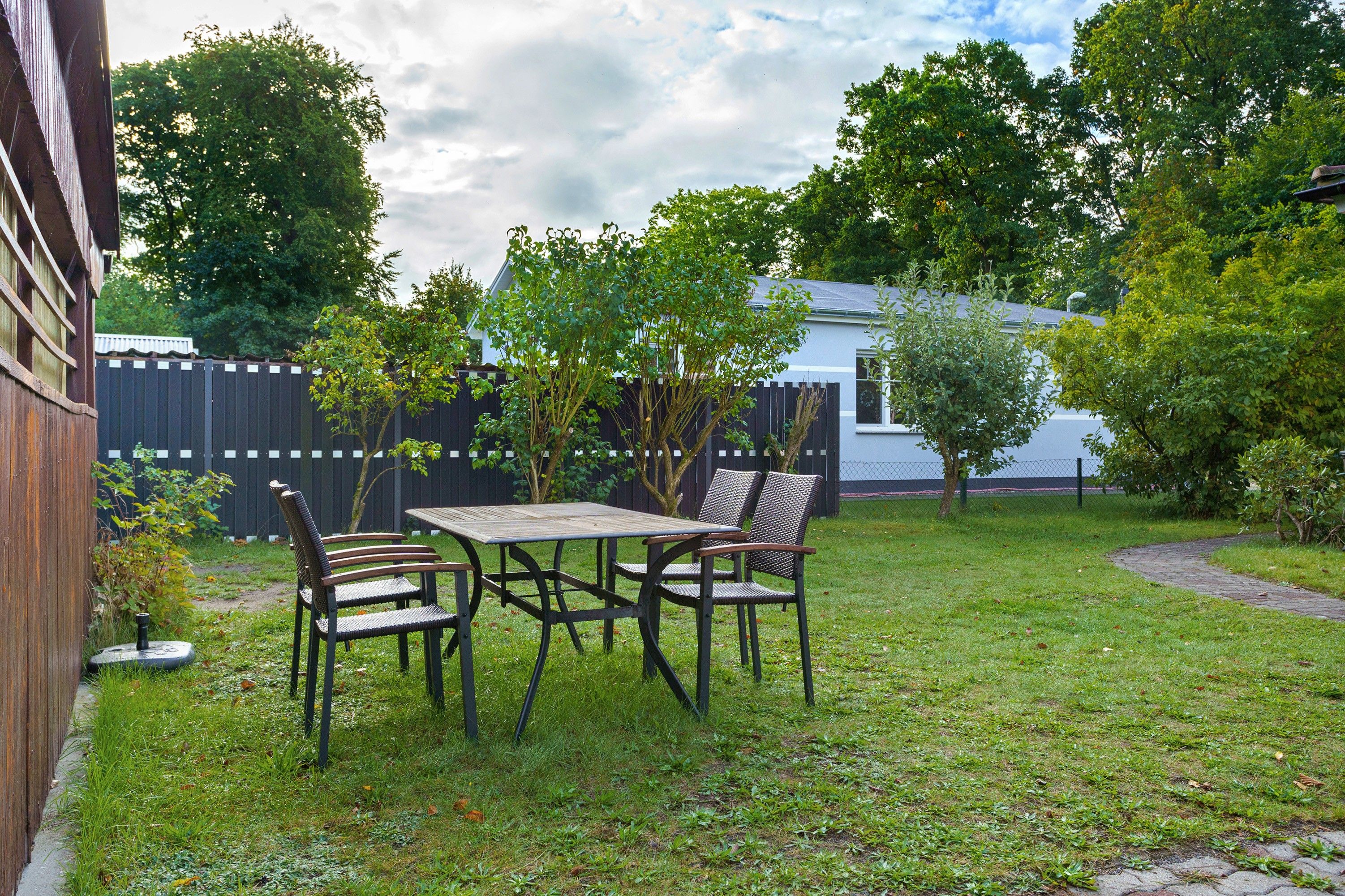 A backyard with a wooden table and two chairs, surrounded by grass and trees.