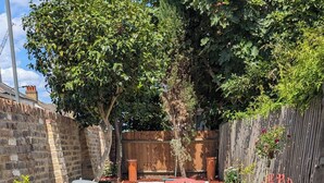 A patio with a table and chairs, surrounded by potted plants and a brick wall. - Spacious three bedroom house with garden, close to O2, quick to central London (London)